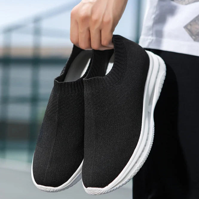 Black slip-on sports shoes held by a person with a blurred background