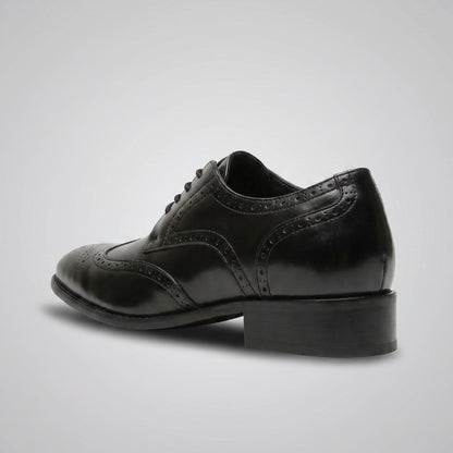 FORCIANO BROGUE black premium leather elevator dress shoe in rear three-quarter view, showing the heel and decorative brogue perforations.