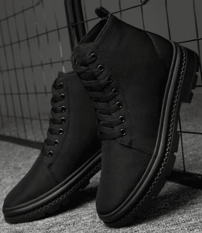 Pair of FORCIANO FORTITUDE black elevator boots displayed in a dark lifestyle setting from a front three-quarter angle.