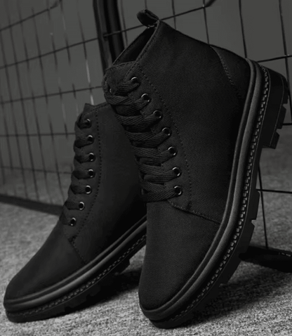 Pair of FORCIANO FORTITUDE black elevator boots displayed in a dark lifestyle setting from a front three-quarter angle.