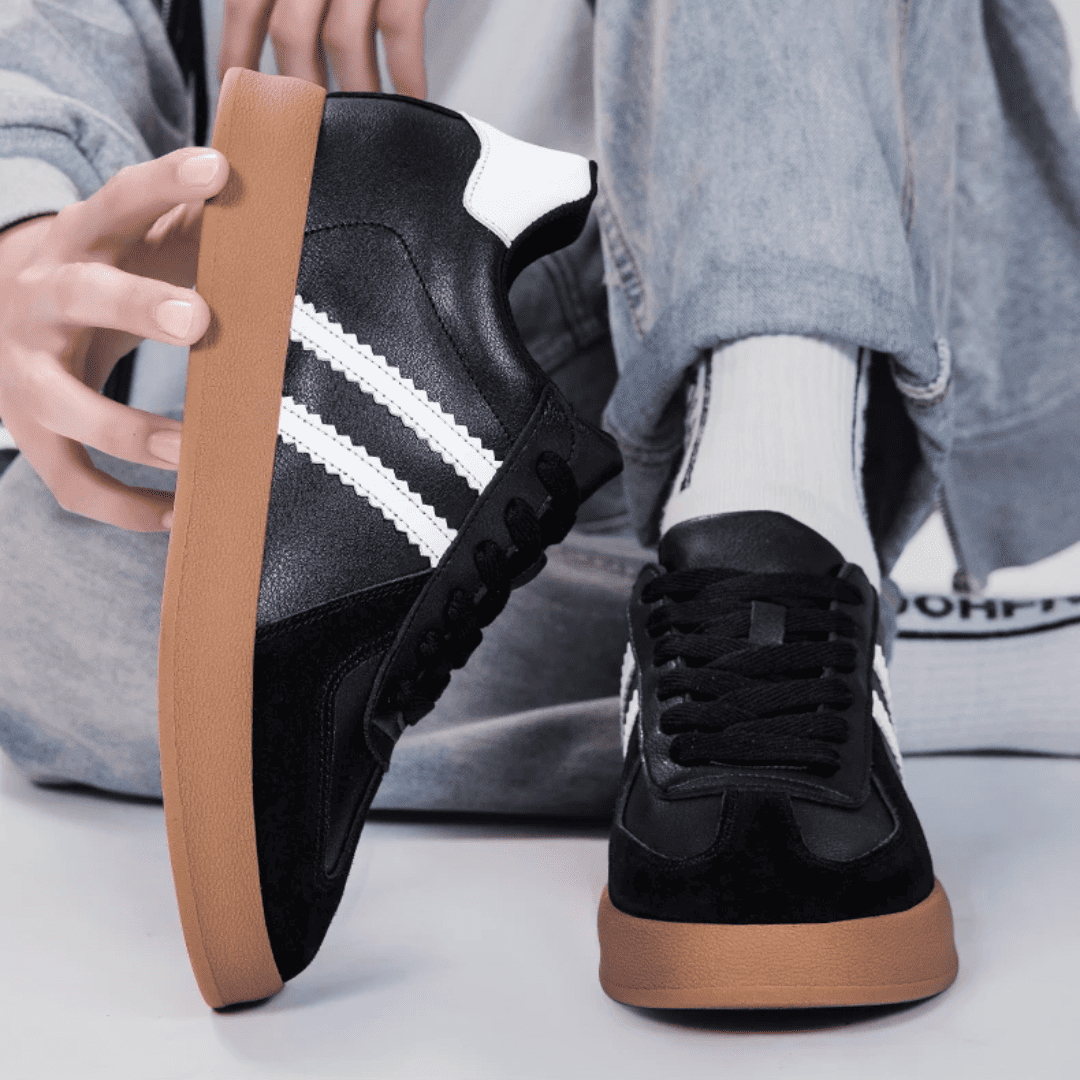 FORCIANO SABER black height increasing sneakers with white stripes and split leather uppers shown worn and held by hand in a casual detail view.