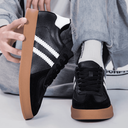 FORCIANO SABER black height increasing sneakers with white stripes and split leather uppers shown worn and held by hand in a casual detail view.