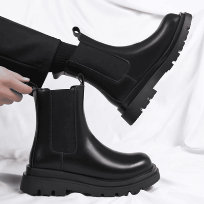 FORCIANO SENTINEL black elevator Chelsea boots shown as a pair, with one worn and one held, highlighting the elastic side panels and premium leather uppers.