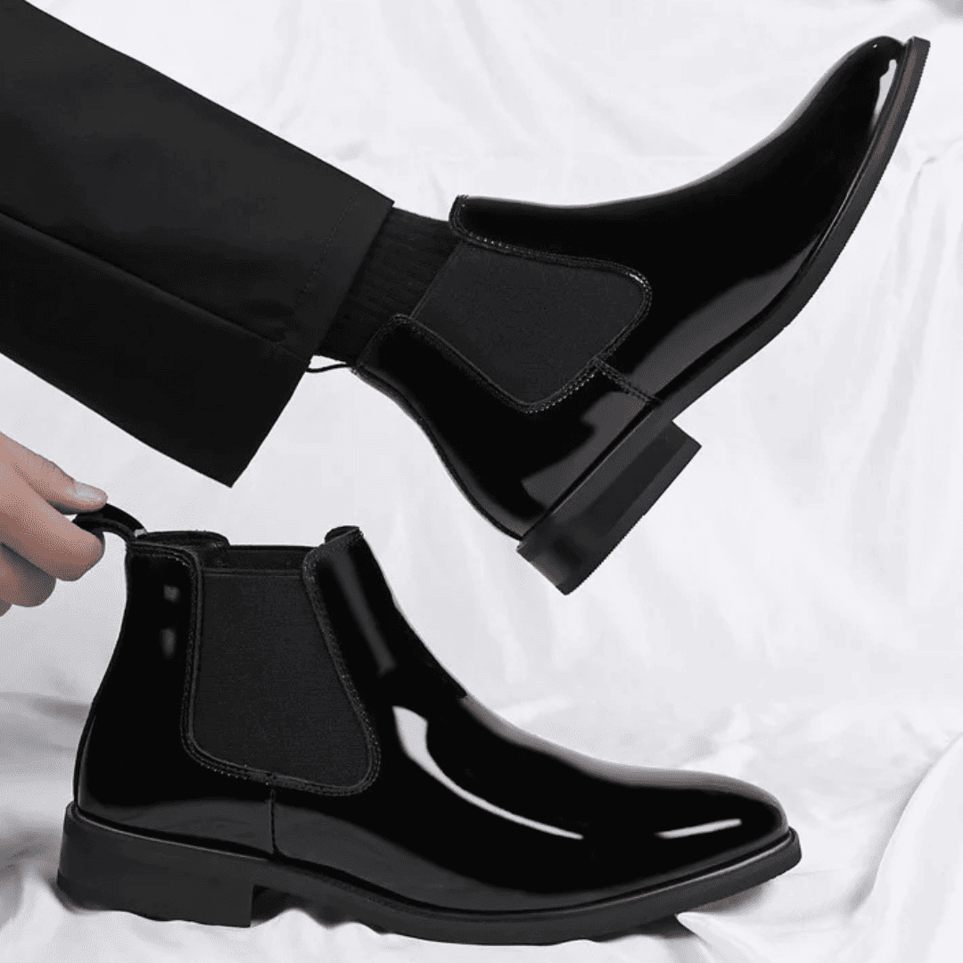 FORCIANO SILVAN black Chelsea Height Increasing Boots shown in a lifestyle view, with one boot worn and the second held by its pull tab.