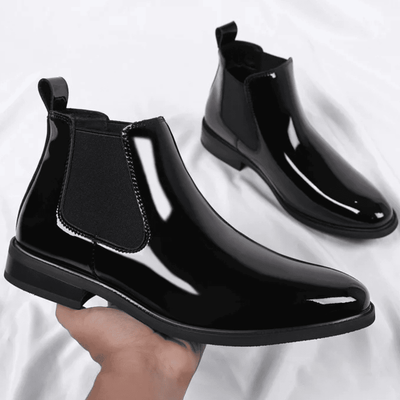 FORCIANO SILVAN black height increasing boots shown as a glossy pair, with one boot held in hand and the second positioned behind.